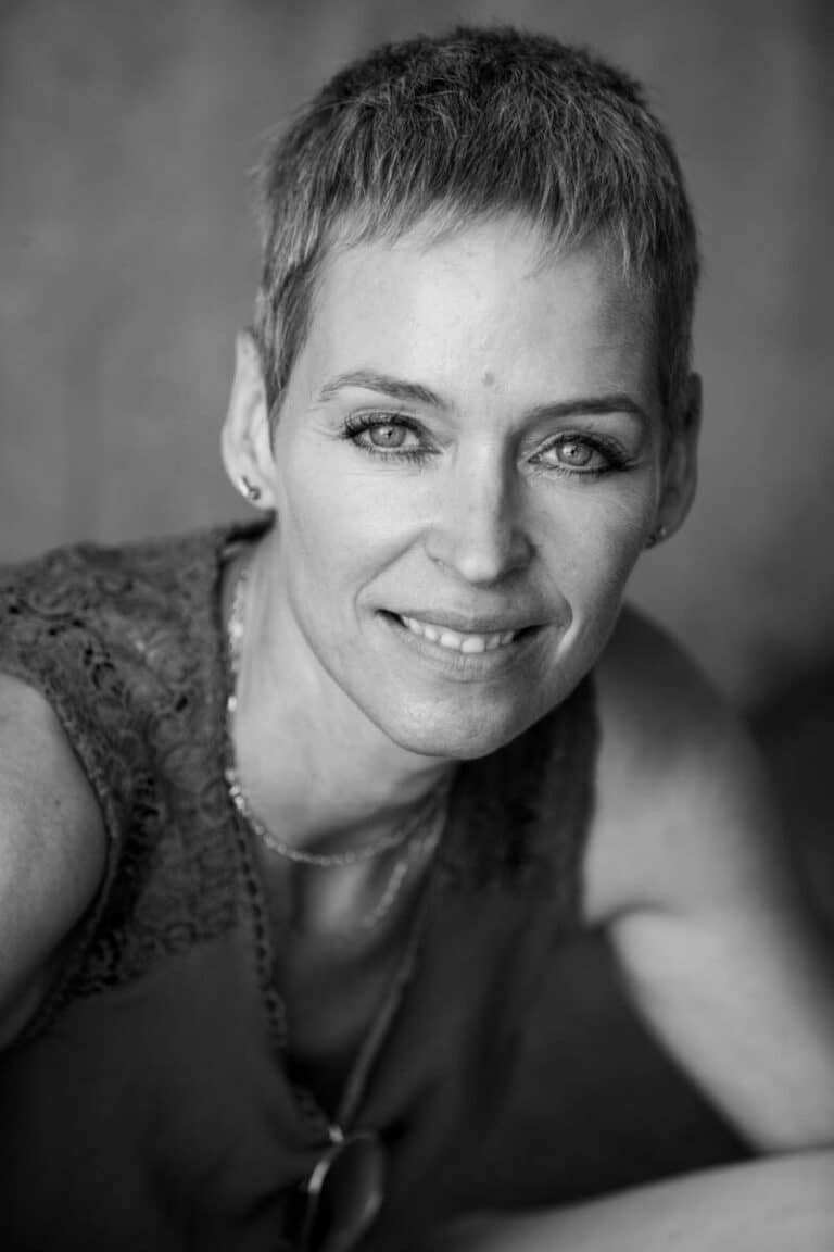 Portrait en noir et blanc d'une femme aux cheveux courts et texturés, aux yeux clairs et au léger sourire. Idéale pour une photo de tournage ou un portfolio de mannequin, cette image de photographe Lyon la représente en dentelle sur un fond flou, mettant en valeur son visage expressif.